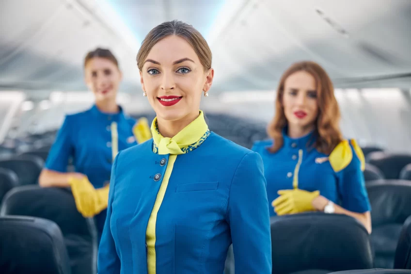 Three cabin crew members standing inside an aircraft looking at the camera and smiling.